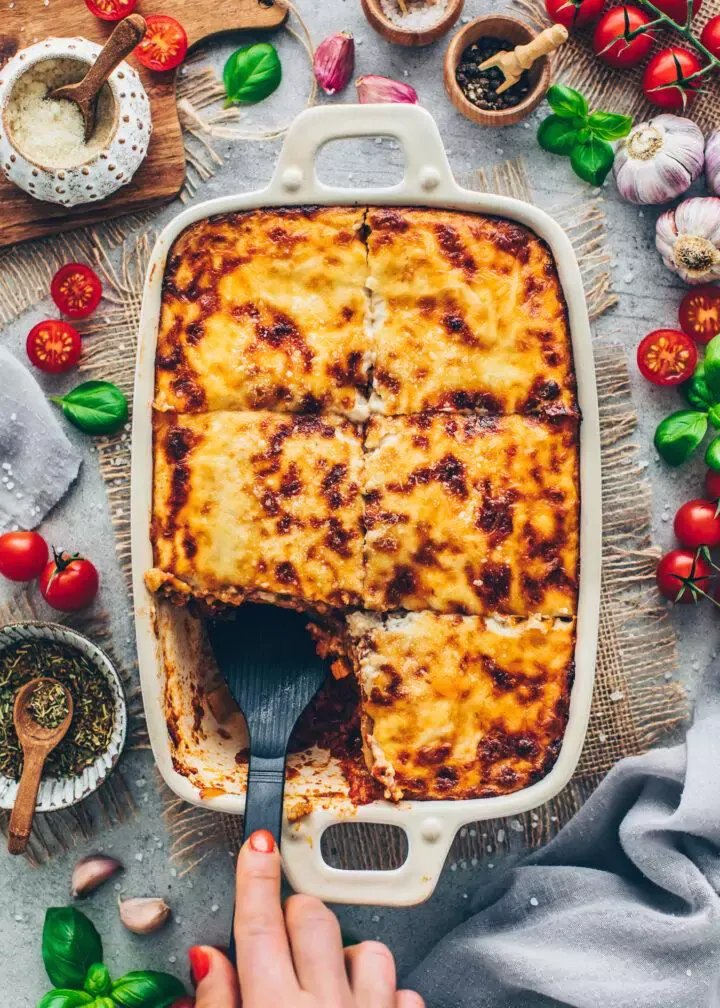 Nahaufnahme einer reichhaltigen Scheibe veganer Lasagne mit sichtbaren Schichten von Nudeln, veganer Bolognese und cremiger Béchamelsauce.