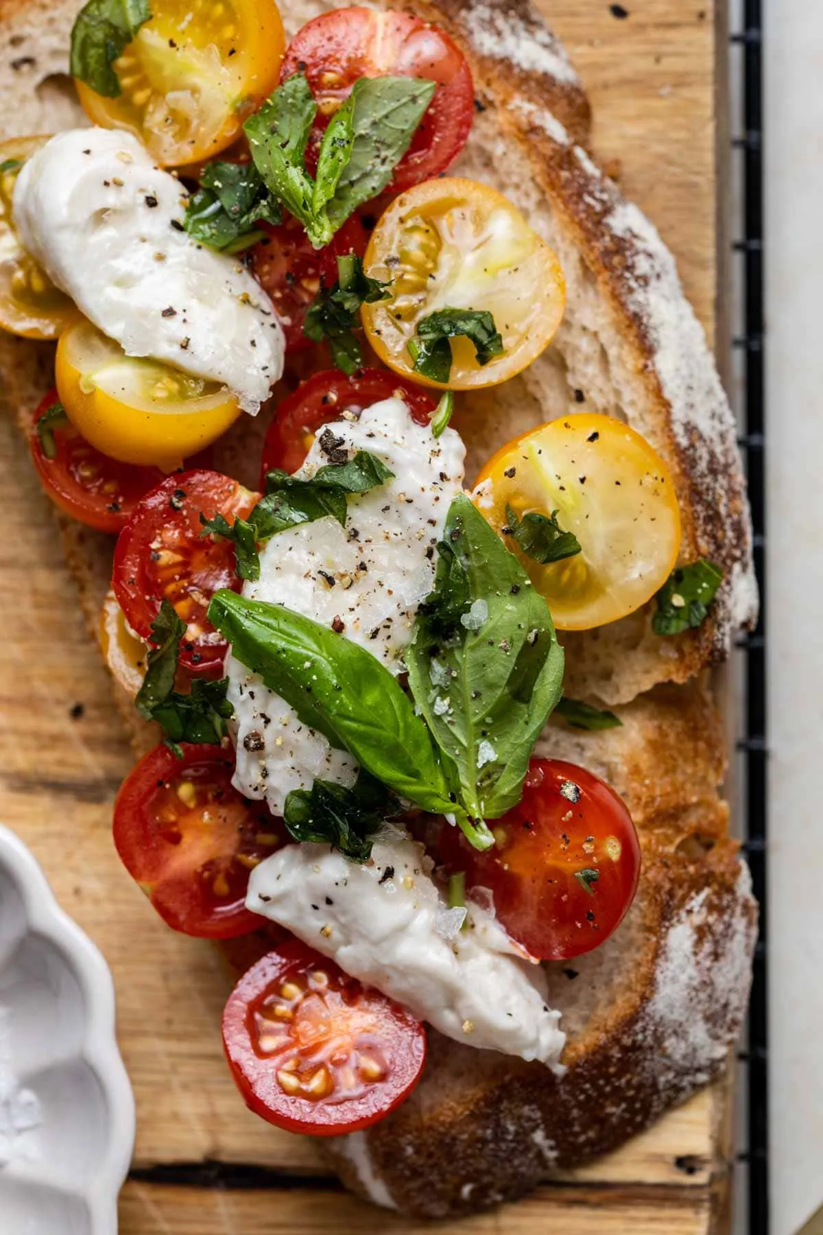 Nahaufnahme einer Scheibe gerösteten Sauerteigbrots mit veganer Burrata, frischen Tomaten und Basilikum.