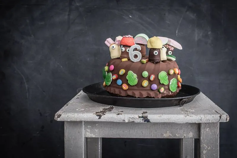 Nahaufnahme eines angeschnittenen Stücks saftigen Marmorkuchens, verziert mit einer Schokokuss-Figur, Zuckeraugen und einem Schaumzuckerhut.