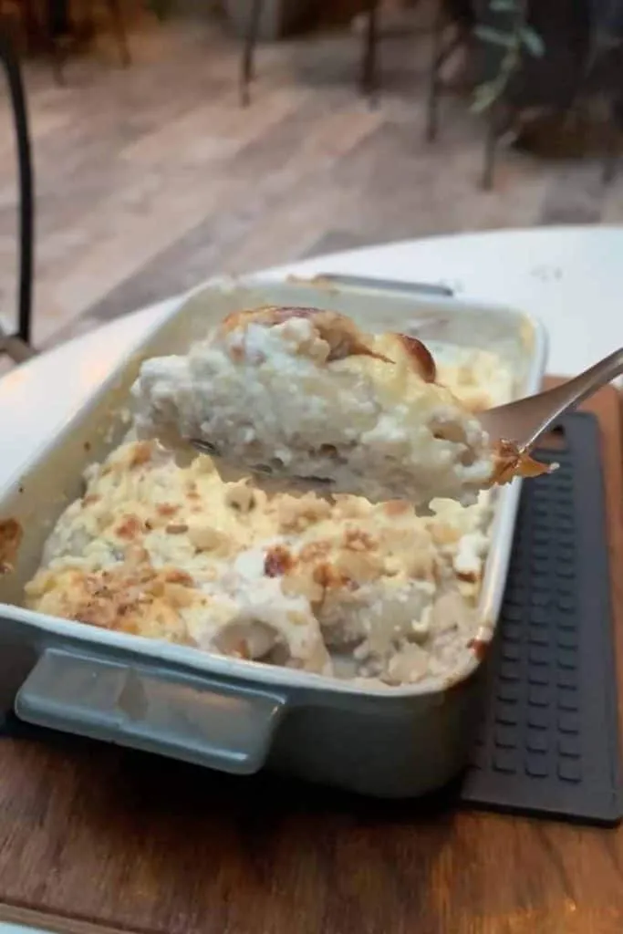 Nahaufnahme eines cremigen, gebackenen Štrukli-Gerichts von La Štruk in Zagreb, mit goldbrauner Kruste, serviert in einer Keramikbackform auf einem Holztisch, ein traditionelles Gericht aus Zagreb.