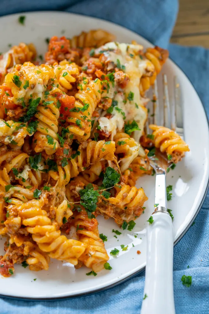 Nahaufnahme eines cremigen Nudelauflaufs mit Hackfleisch und geschmolzenem Käse, verziert mit frischen Kräutern.