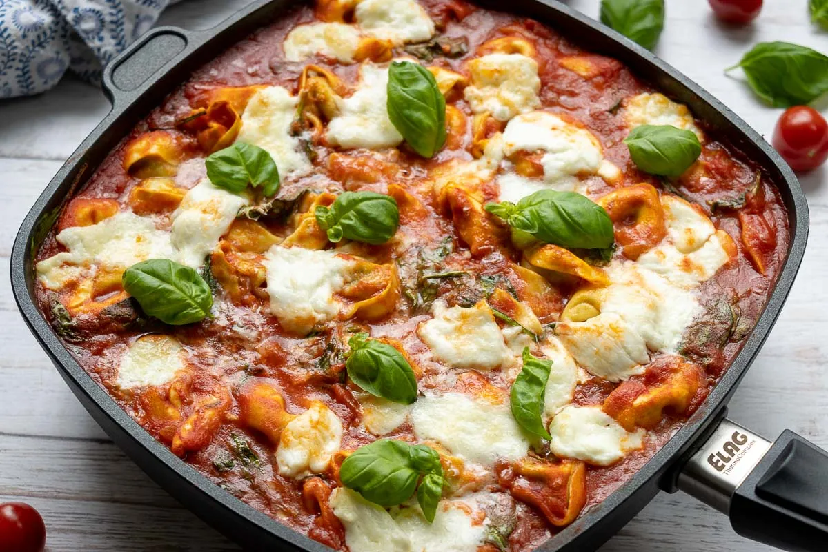Nahaufnahme eines cremigen Tortellini Auflaufs mit Spinat und geschmolzenem Käse, angerichtet in der Pfanne