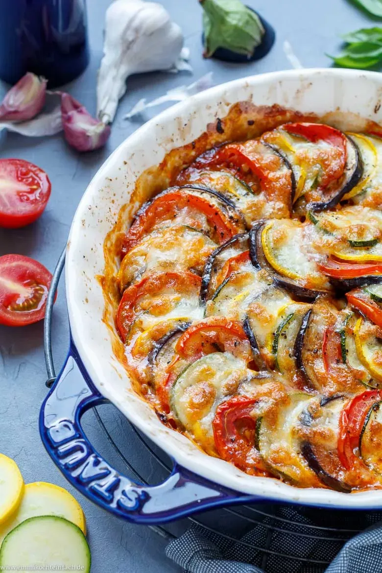 Nahaufnahme eines geschichteten Zucchini-Aubergine-Auflaufs vor dem Backen, mit Mozzarella bestreut.