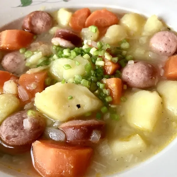 Nahaufnahme eines herzhaften Eintopfs mit Bockwurst, Kartoffeln und Karotten, garniert mit Frühlingszwiebeln