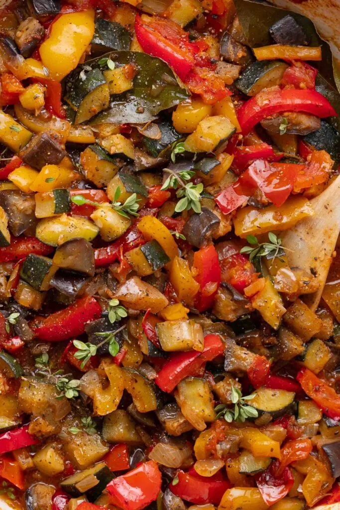 Nahaufnahme eines Ratatouille, das aus gewürfelten Zucchini, Auberginen, Paprika, Tomaten und Kräutern gekocht und mit einem Holzlöffel vermengt wurde.