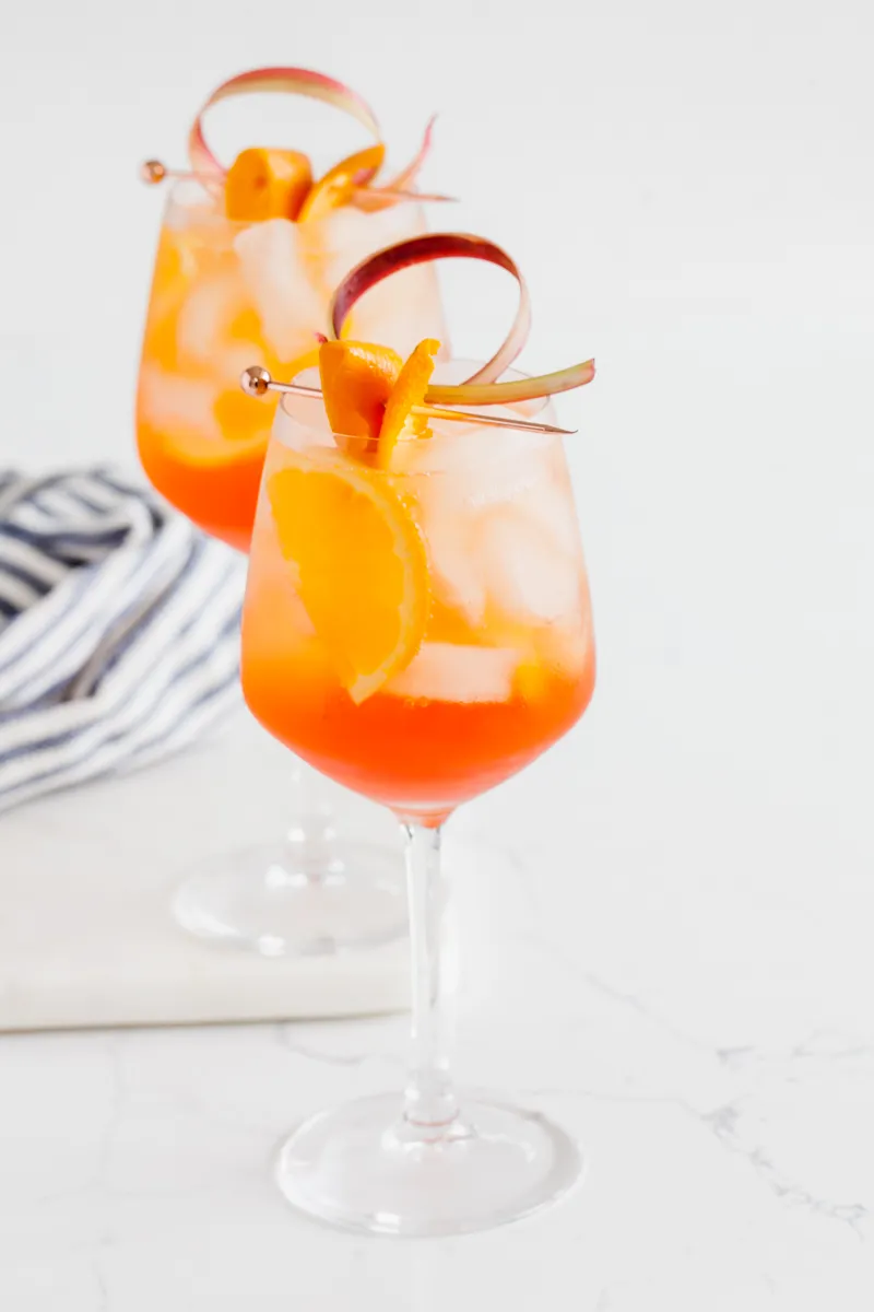 Nahaufnahme eines Rhabarber Aperol Spritz mit Eiswürfeln und Rhabarberdekoration in einem Weinglas.