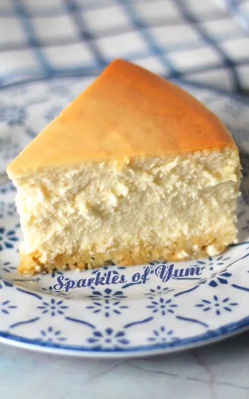 Nahaufnahme eines Stücks New York Cheesecake auf einem blau-weißen Teller, das die dichte Textur zeigt.