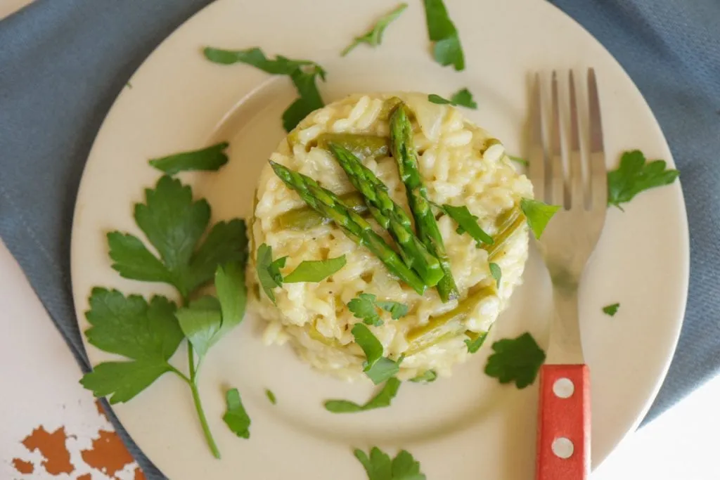 Nahaufnahme eines Tellers mit veganem Spargelrisotto, garniert mit frischen Kräutern und Spargelspitzen. Der Reis ist cremig und leicht glänzend, was auf die perfekte Konsistenz hinweist.