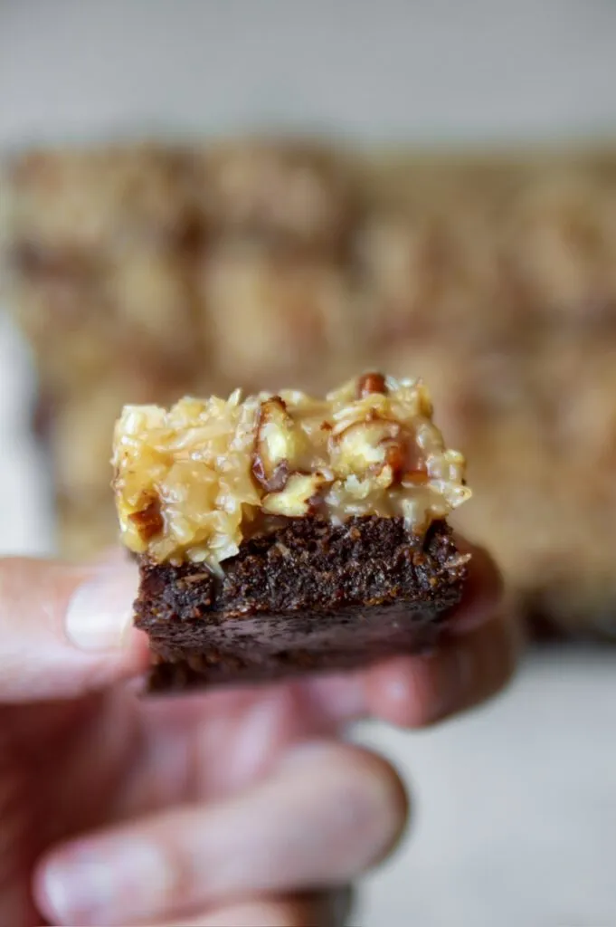 Nahaufnahme eines veganen Brownies mit glänzendem Kokos-Pekan-Topping, der auf einem Teller liegt.