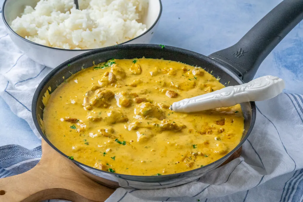 Nahaufnahme von cremigem Curry-Geschnetzeltem in einer Pfanne, kurz vor dem Servieren