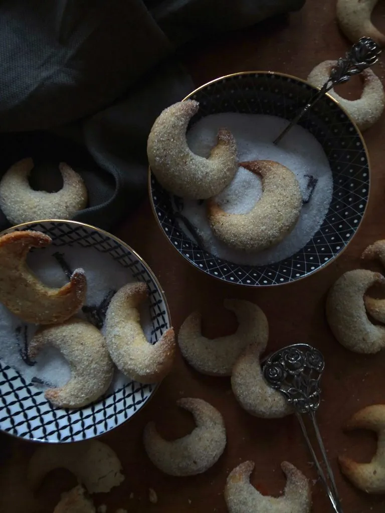 Nahaufnahme von goldbraunen Vanillekipferl, die leicht mit Vanillezucker bestäubt sind, auf einer Kuchenplatte angerichtet