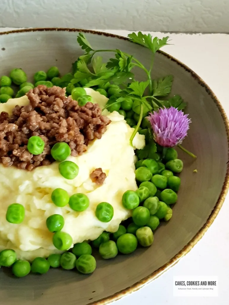 Nahaufnahme von Kartoffelbrei mit Hackfleisch und Erbsen auf einem Teller, dampfend und appetitlich angerichtet