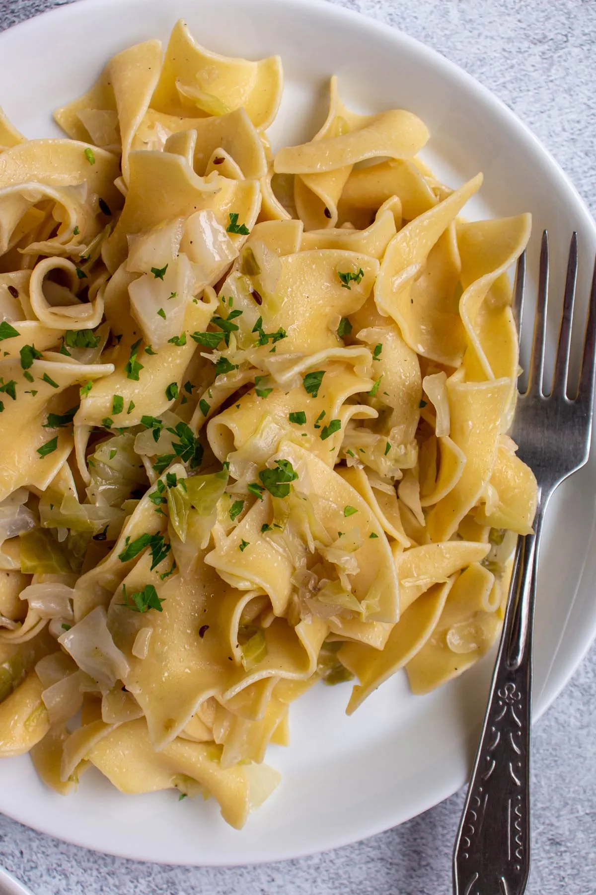 Nahaufnahme von Krautfleckerl mit gehackter Petersilie auf einem weißen Teller mit Gabel.