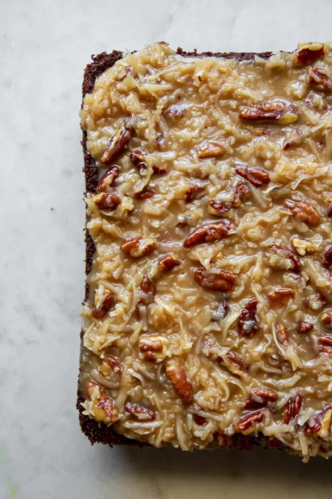 Nahaufnahme von veganen Brownies mit Kokos-Pekan-Topping, die auf einem Holzteller gestapelt sind.