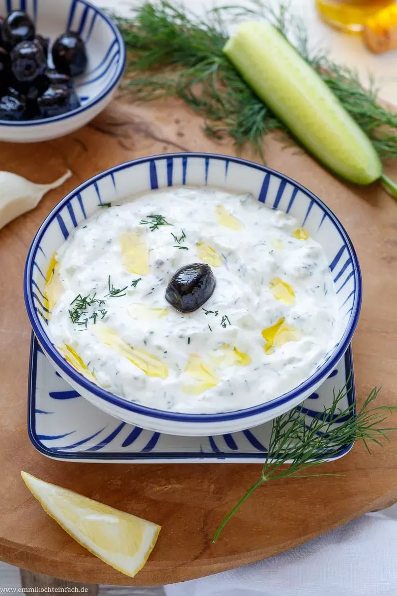 Nahaufnahme von Zaziki mit einem Löffel, umgeben von frischen Zutaten wie Gurke, Knoblauch und Dill