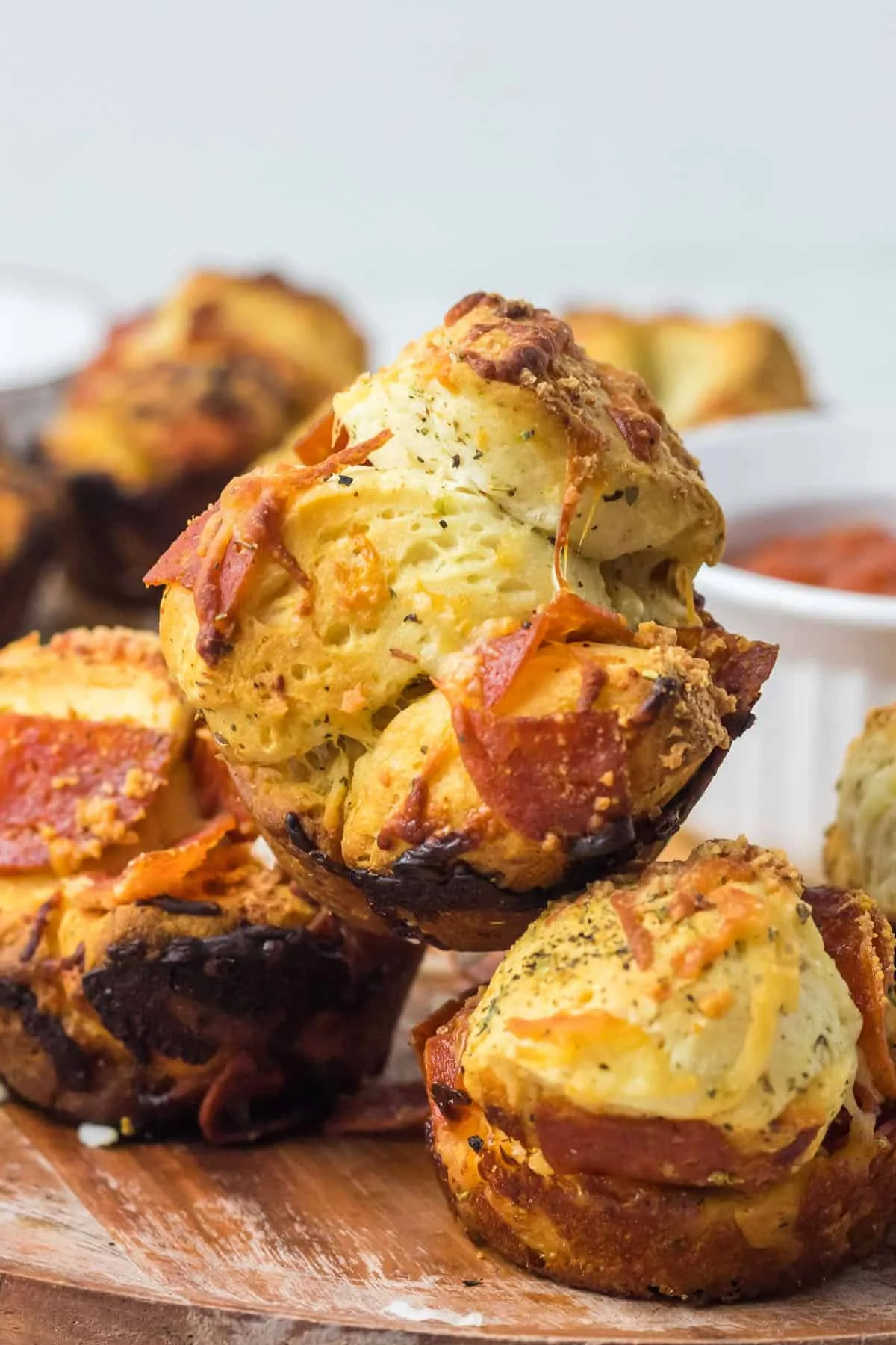 Nahaufnahme von zwei Pizza Muffins, einer davon ist zerbrochen und zeigt die Füllung, auf einem Holzbrett mit einer Schale Marinara.