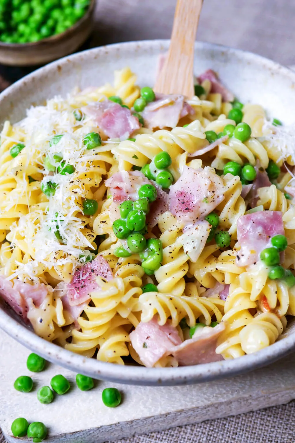 Nudeln mit Schinken-Sahne-Sauce und Erbsen in der Schüssel. Alternative Text: Cremige Nudeln mit Schinken-Sahne-Sauce, angereichert mit grünen Erbsen, serviert in einer weißen Schüssel, ein herzhaftes und schnelles Mittagessen.