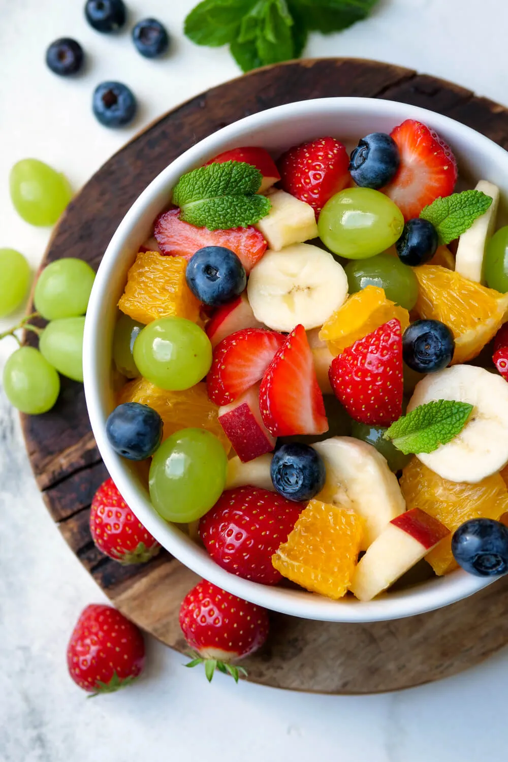Obstsalat mit Orangen, Weintrauben, Erdbeeren, Banane, Heidelbeeren und Apfel in der Schüssel