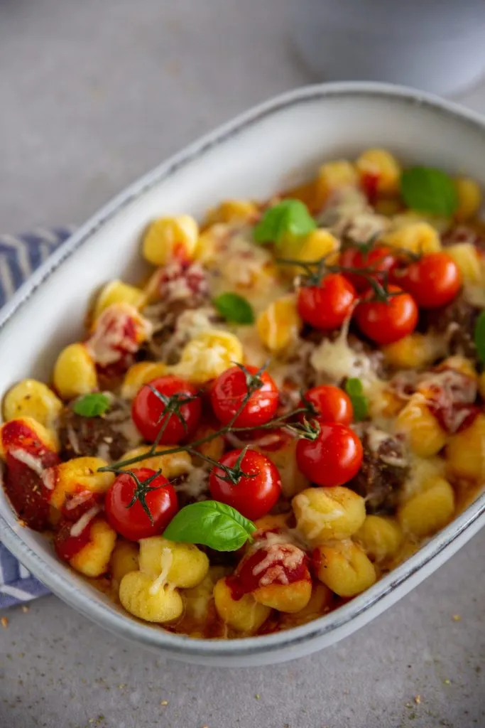 Ofen-Gnocchi mit Hackbällchen, die in einer roten Tomatensauce schwimmen, mit frischen Kräutern bestreut und dampfend heiß serviert werden.