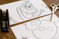 Olaf-Schablone auf einem Backblechkuchen positioniert, vorbereitend für den Zuschnitt des beliebten Schneemanns.