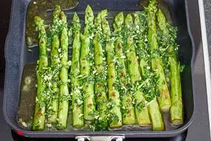 Ölivenöl mit Kräutern in die Pfanne über den grünen Spargel gießen