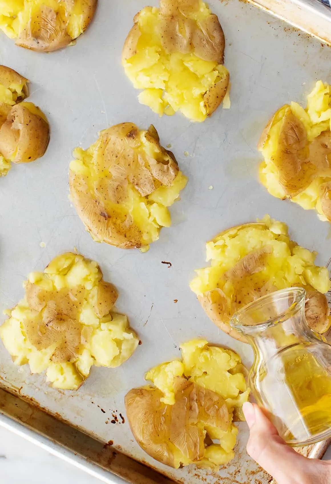 Olivenöl wird über die zerdrückten Kartoffeln auf dem Backblech geträufelt
