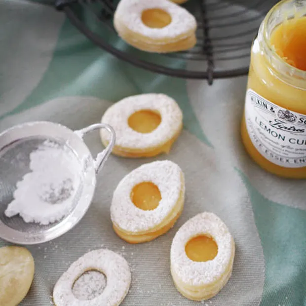 Osterplätzchen mit Lemon Curd: Eierförmige Kekse, liebevoll mit Puderzucker bestreut und fruchtiger Zitronencreme gefüllt, ein Highlight für jede Osterkaffeetafel.