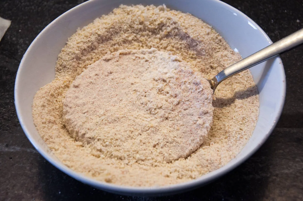 Paniertes Kohlrabi-Schnitzel, bereit zum Frittieren, auf einem Schneidebrett arrangiert