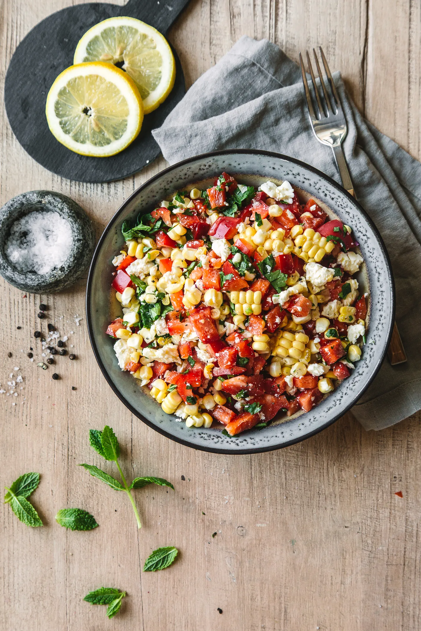 Paprika-Mais-Salat in Schüssel mit Besteck und Zitrone auf Tisch