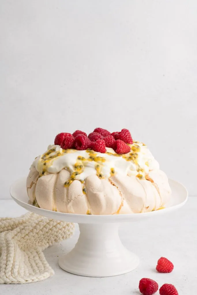 pavlova auf weißem Kuchenständer mit Schlagsahne, Maracuja und Himbeeren