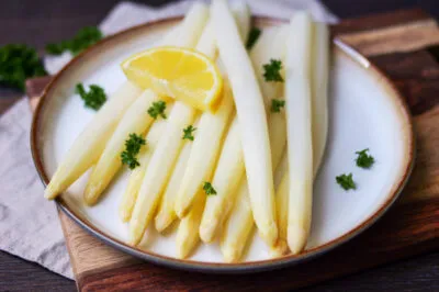 Perfekt gekochter weißer Spargel mit Zitrone und Petersilie auf einem Teller, servierfertig.