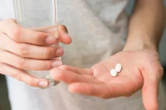 Person hält Pillen und Glas Wasser in Händen