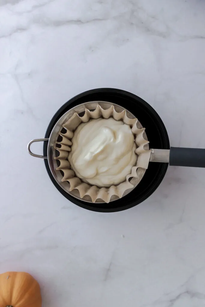 Pflanzlicher Joghurt wird in ein Sieb mit Kaffeefilter gegeben