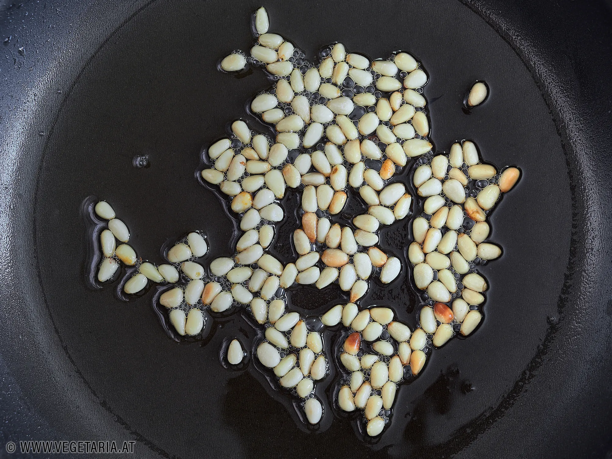 Pinienkerne werden in einer Pfanne goldbraun geröstet.