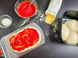 Pinsa-Fladen auf dem Pizzaschieber mit Tomatensauce bestreichen