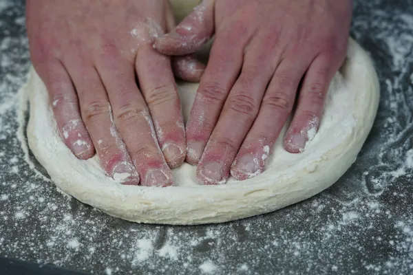 Pizzateig mit flachen Händen ausbreiten