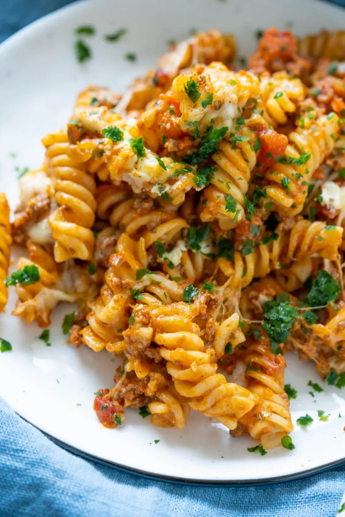 Portion Nudelauflauf mit Hackfleisch auf einem Teller, daneben eine Auflaufform, bereit für weitere Portionen des beliebten Gerichts.