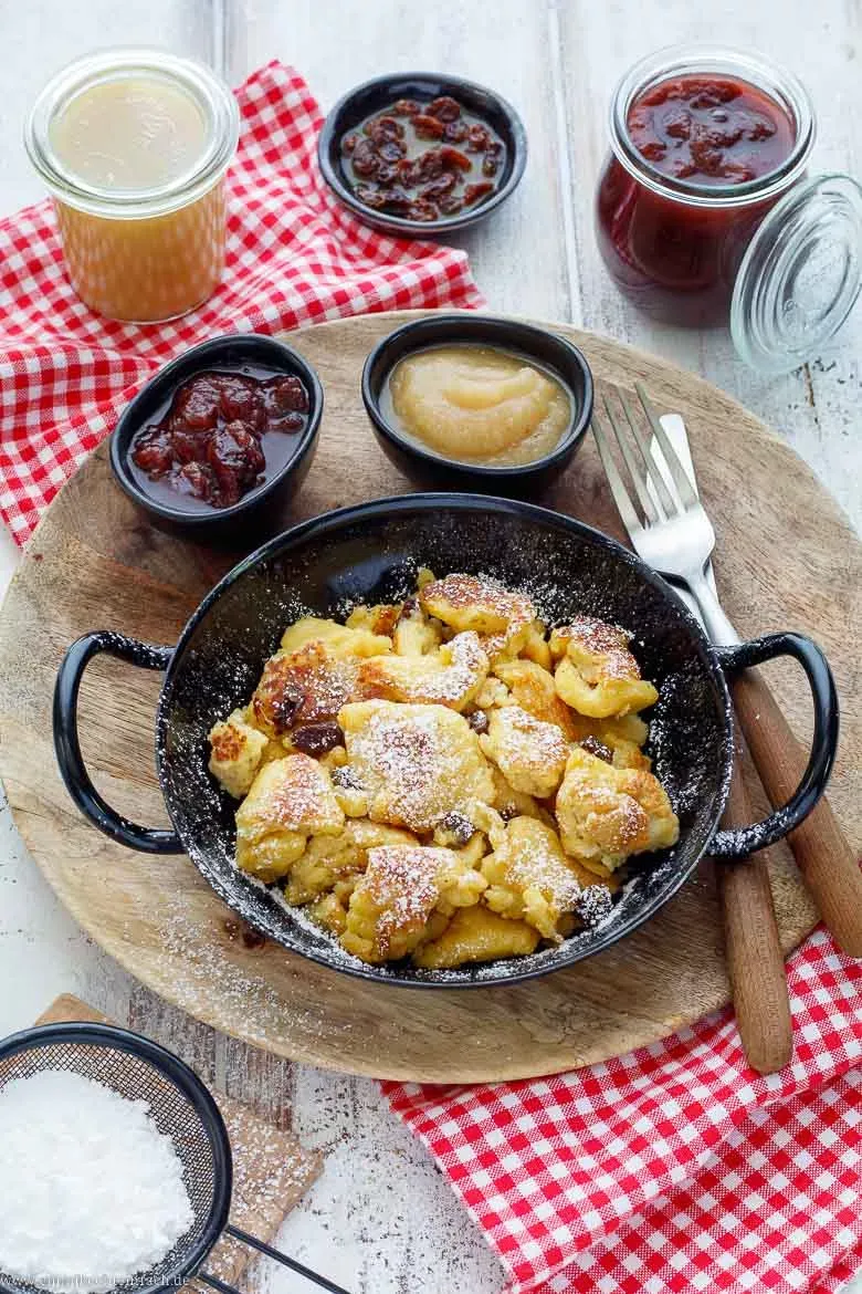 Portionen von goldbraunem, fluffigem Kaiserschmarrn auf einem Teller, liebevoll mit Puderzucker bestäubt und bereit zum Genuss. Perfektes Kaiserschmarrn selber machen für die Familie.