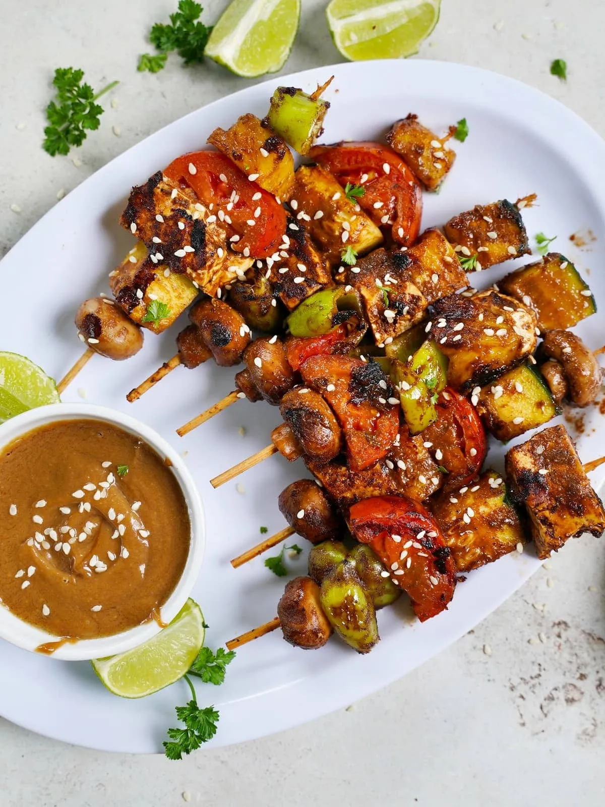 Proteinreiche vegane Tofu-Gemüsespieße in BBQ-Marinade mit Erdnusssauce auf einer weißen Platte, ideal für Grillabende oder Mittagessen.