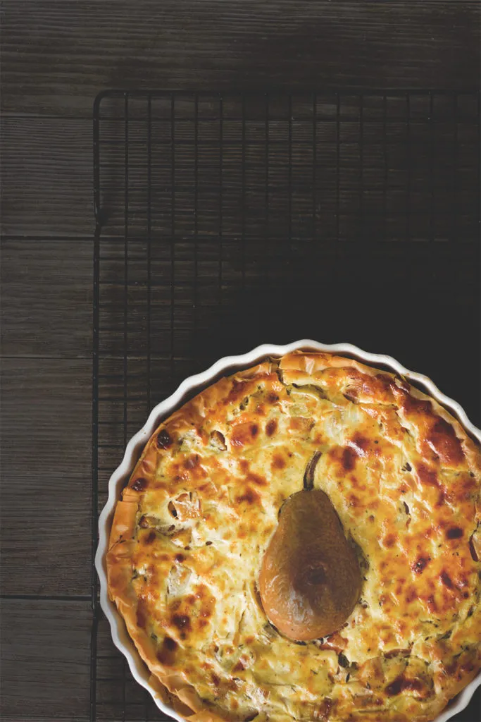 Quiche mit Kürbis, Lauch und Birne auf einer Holzplatte mit einem Stück herausgeschnitten