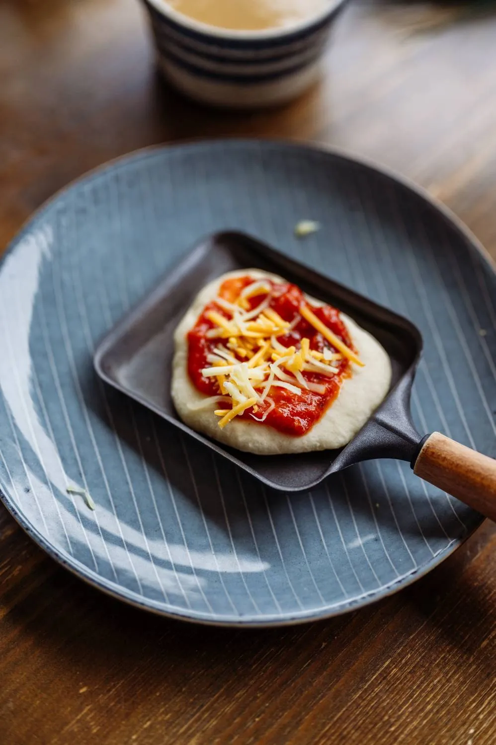 Raclette-Pfännchen mit vorgebackenem Pizzateig und Tomatensauce als Basis für Mini-Pizzen