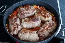 Rinderrouladen schmoren in einer würzigen Soße zusammen mit Gemüse in einem Bräter im Ofen.