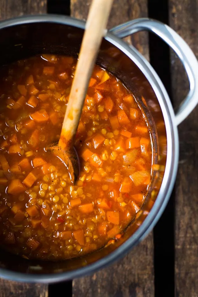 Rote Linsensuppe köchelt in einem schwarzen Topf, mit Gewürzen und Gemüse