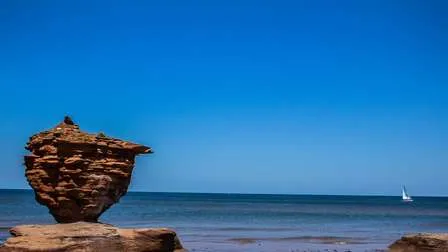 Rote Sandstrände und Gesteinsformationen an der Küste der Prinz-Edward-Insel, Kanadas kleinster Provinz, unter blauem Himmel.