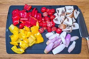 Rote und gelbe Paprika in größere Würfel schneiden, die Kirschtomaten in Hälften und die Champignons in Viertel schneiden. Schalotten schälen und halbieren.