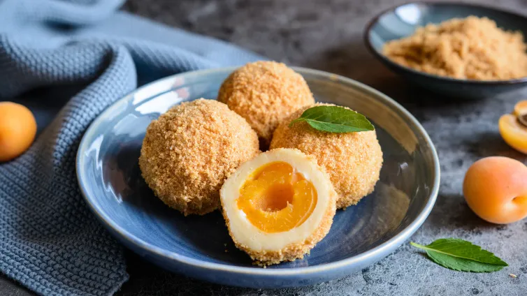 Saftige Marillenknödel mit Quarkteig, umhüllt von gerösteten Bröseln und Puderzucker, ein süßes Highlight der österreichischen Küche.