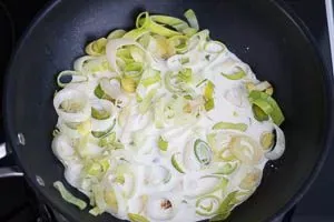 Sahne und Milch zu den angedünsteten Lauchzwiebeln in die Pfanne gießen