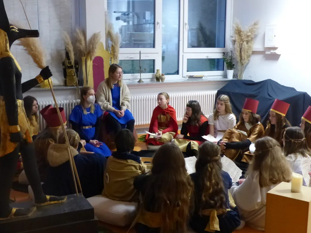 Schülerinnen in antiken Gewändern lesen und forschen an Tischen