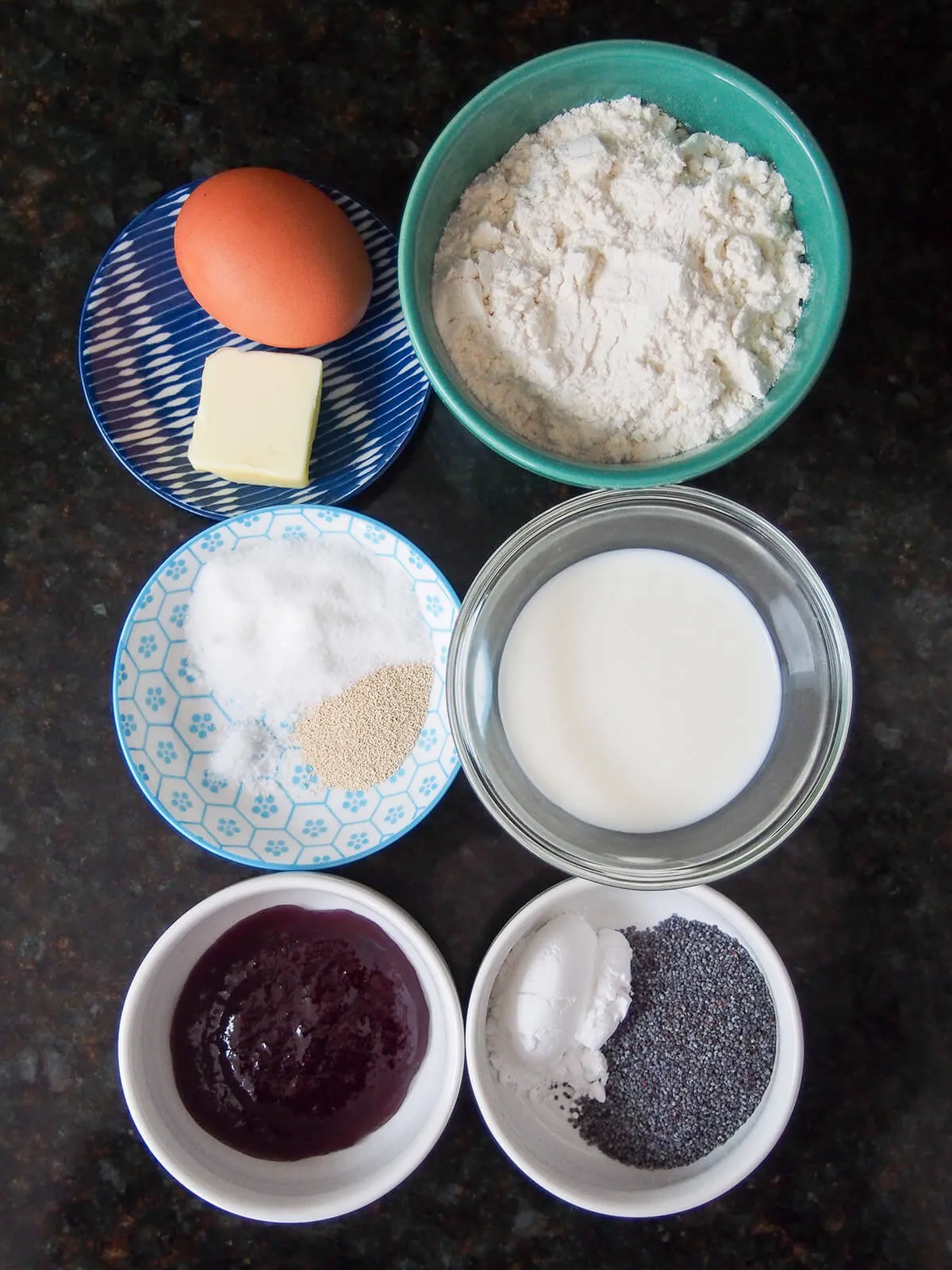 Schüsseln mit Mehl, Milch, Zucker, Marmelade, Mohn, Ei und Butter.