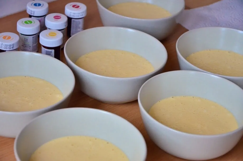 Sechs Schüsseln mit weißem Biskuitteig, bereit zum Einfärben für die farbenfrohe Torte